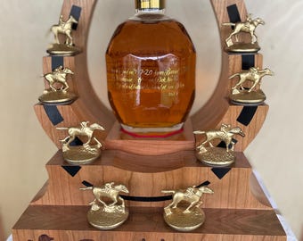 May include: A whiskey bottle with a gold horse and jockey stopper, presented on a wooden stand with gold horse and jockey figurines. The stand features a horseshoe design and the word "Double !!" is engraved on the base.