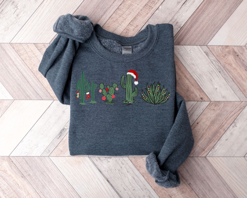 May include: A dark gray sweatshirt with a Christmas cactus design. The cactus is wearing a Santa hat and has Christmas lights and ornaments on it.