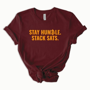 May include: Burgundy t-shirt with the text "STAY HUMBLE. STACK SATS." in orange.