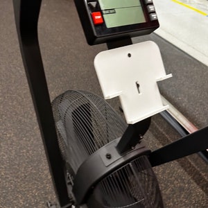May include: Black and white exercise bike with a digital display and a white phone holder. The bike has a large fan in the back.