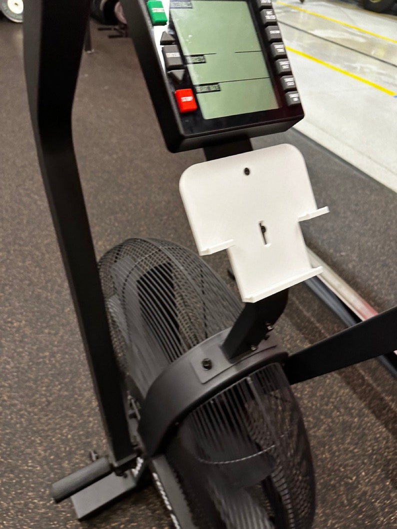 May include: Black and white exercise bike with a digital display and a white phone holder. The bike has a large fan in the back.