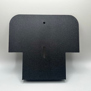May include: Black plastic wall mount with a rounded top and a rectangular opening in the center. The mount has a textured surface.