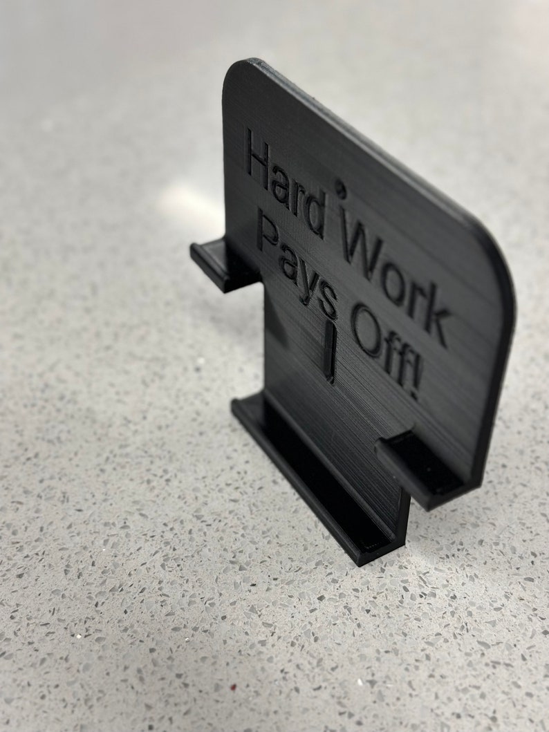 May include: Black 3D printed sign with the text "Hard Work Pays Off!" The sign is designed to stand upright on a flat surface.