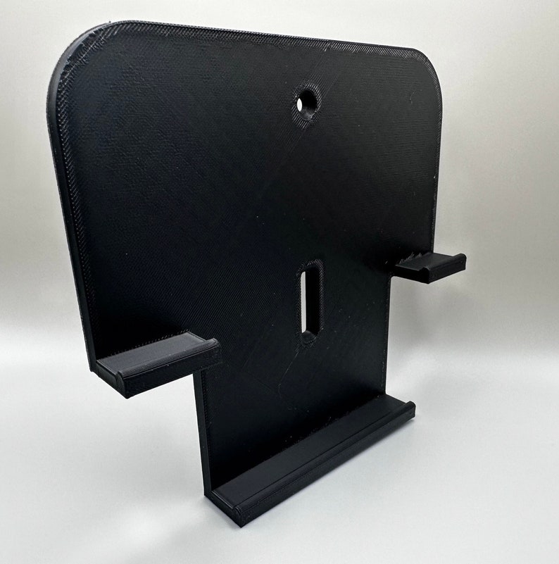 May include: Black plastic wall mount with two slots for holding controllers and a shelf for a console.