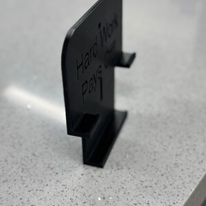 May include: Black plastic sign with the text "Hard Work Pays Off" in white lettering.