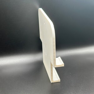 May include: White plastic wall mount phone holder with a single slot for a phone. The holder has a rounded edge and a smooth surface.