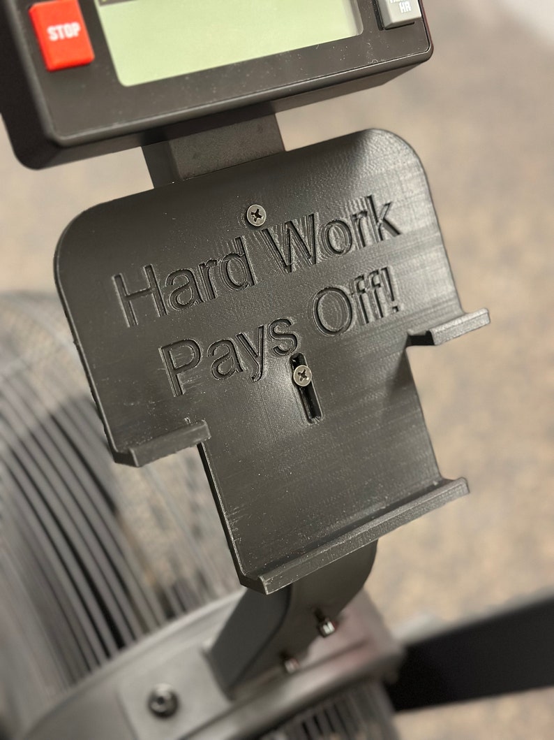 May include: A black 3D printed sign with the text "Hard Work Pays Off!" mounted on a black exercise machine.