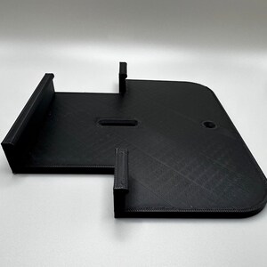 May include: Black plastic 3D printed wall mount with two slots and a hole.