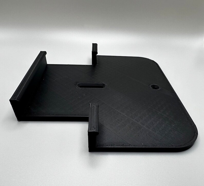 May include: Black plastic 3D printed wall mount with two slots and a hole.