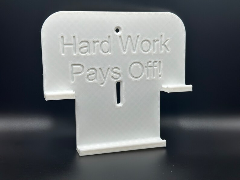 May include: White plastic wall mount with the text "Hard Work Pays Off!" printed on it. The mount has two slots for holding items.