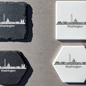 May include: Four coasters featuring a white outline of the Washington D.C. skyline with the word "Washington" below. Two coasters are black slate and two are white ceramic. One of the white ceramic coasters is a hexagon shape.