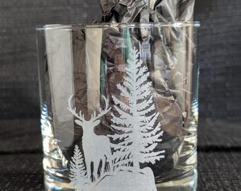 May include: A clear glass tumbler with an etched design of a deer standing in a forest. The deer is silhouetted against a white background.