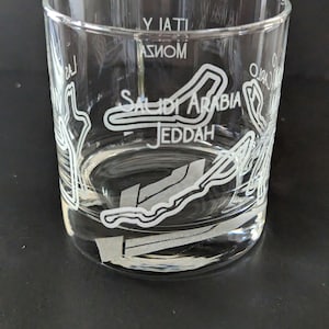 May include: A clear glass tumbler with an etched design of the Jeddah street circuit, featuring the text "Saudi Arabia Jeddah" and "Yati Asom".