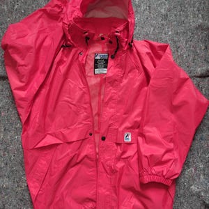May include: A bright pink K-Way 2000 Active Outdoor Wear jacket with a zip fastening and a hood. The jacket has a logo patch on the left sleeve.