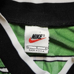 May include: Close-up of a green and white striped jersey with a black collar and white trim. The Nike logo is visible on a tag that reads "MADE IN U.S.A."