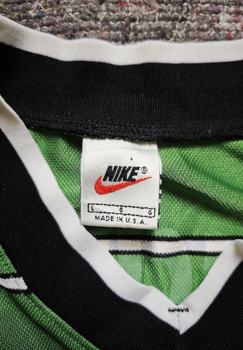 May include: Close-up of a green and white striped jersey with a black collar and white trim. The Nike logo is visible on a tag that reads "MADE IN U.S.A."