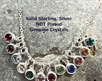 May include: A silver chain necklace with multiple charms, each featuring a different colored crystal. The charms are round and dangle from the chain. The necklace is on a gray stone background. The text "Solid Sterling: Silver NOT Plated Genuine Crystals" is visible on the image.
