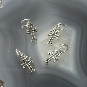 May include: Four silver cross charms with intricate designs. The charms are small and delicate, perfect for adding a touch of faith to jewelry.