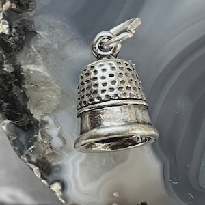 May include: A silver thimble charm with a textured surface and a loop for attaching to a chain or bracelet.