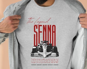 Puede incluir: Una camiseta gris con una imagen en blanco y negro de un coche de carreras y el texto "The Legend SENNA" en rojo. La cita "No tengo sueños en mi coche, están en mi cabeza, pero van de la mano. Es imposible mirar hacia atrás, porque si te pierdes y te atascas, no puedes vencer a la humanidad. Eso es..." está impresa debajo de la imagen.