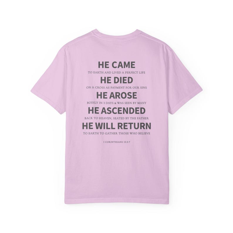 May include: A light pink t-shirt with the text "HE CAME...HE WILL RETURN" in gray. The text is a religious message from 1 Corinthians 15:3-7. The shirt is a short-sleeved crew neck.