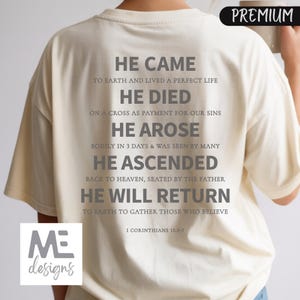 May include: Cream-colored t-shirt with gray text. The text reads "HE CAME, HE DIED, HE AROSE, HE ASCENDED, HE WILL RETURN" with related phrases. The shirt also features the text "I Corinthians 15:3-7" and the "ME designs" logo.