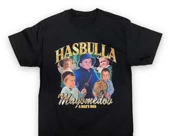 May include: Black t-shirt with a graphic print of a group of children. The graphic features the text "Hasbulla Magomedov" and "A Man's Man".