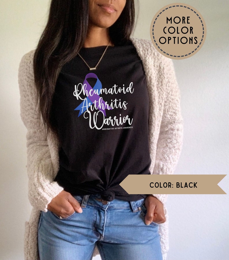 May include: A black t-shirt with a purple and blue ribbon design. The text "Rheumatoid Arthritis Warrior" is printed on the shirt. The hashtag "#rheumatoidarthritisawareness" is printed below the text.