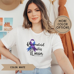 May include: White t-shirt with a purple and blue ribbon design. The text "Rheumatoid Arthritis Warrior" is printed on the shirt.  #rheumatoidarthritisawareness