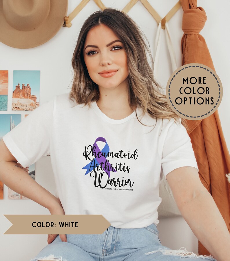 May include: White t-shirt with a purple and blue ribbon design. The text "Rheumatoid Arthritis Warrior" is printed on the shirt.  #rheumatoidarthritisawareness