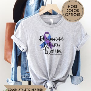 May include: A heather grey t-shirt with a purple and blue ribbon design. The text "Rheumatoid Arthritis Warrior" is printed on the shirt. #rheumatoidarthritisawareness