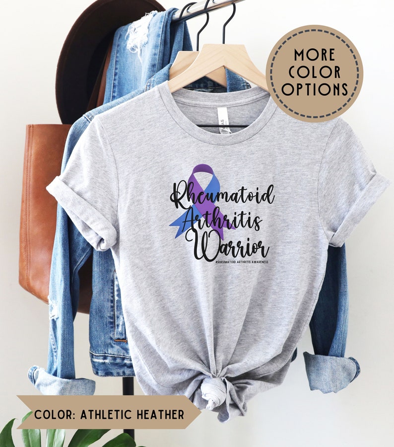 May include: A heather grey t-shirt with a purple and blue ribbon design. The text "Rheumatoid Arthritis Warrior" is printed on the shirt. #rheumatoidarthritisawareness