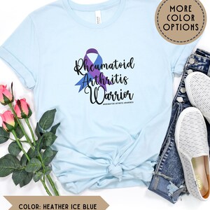 May include: A light blue t-shirt with a purple and blue ribbon and the text "Rheumatoid Arthritis Warrior #RHEUMATOID ARTHRITIS AWARENESS".
