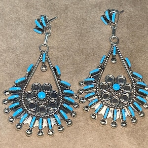 Pode incluir: Um par de brincos de prata pendurados com detalhes em turquesa. Os brincos têm um design circular com uma pedra turquesa menor no centro.