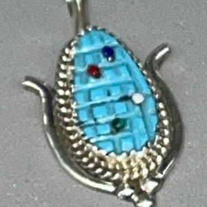 May include: A silver pendant shaped like an ear of corn with turquoise, red, green, and white stones.