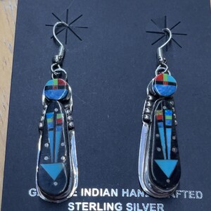 May include: Sterling silver dangle earrings with a black background. Each earring features a geometric design with turquoise, red, blue, and yellow accents. The earrings are labeled "INDIAN HAND CRAFTED STERLING SILVER."