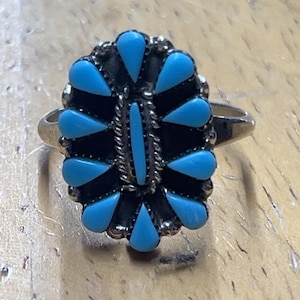 Könnte beinhalten: Ein silberner Ring mit einem floralen Design, besetzt mit tropfenförmigen Steinen in Türkis. Der Ring hat ein detailliertes Band und einen zentralen Türkisstein. Der Ring liegt auf einer Holzoberfläche.