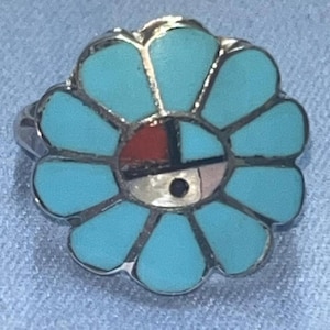 May include: A silver ring featuring a turquoise flower design. The flower petals are a light blue, with a center of red, black, white, and pink. The ring has a detailed, handcrafted appearance.
