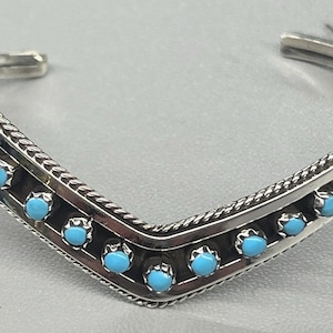 Puede incluir: Un brazalete de plata con un diseño en forma de V y piedras turquesa.