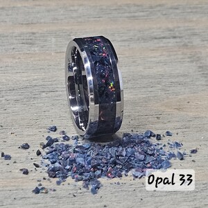 May include: A silver ring with a dark, textured center band containing flecks of color. The ring is next to a pile of small, dark blue and red fragments. The text "Opal 33" is in the lower right corner.