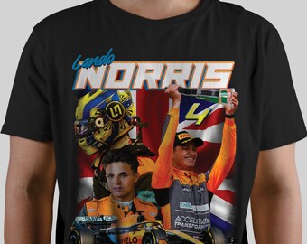Pode incluir: Camiseta preta com um gráfico de Lando Norris, um piloto de Fórmula 1. O gráfico mostra Norris com um macacão de corrida, segurando um troféu, e um close-up de seu capacete. O texto "Lando Norris" é impresso em uma fonte colorida.