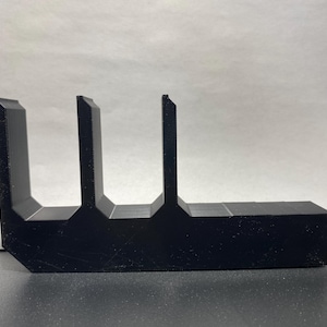 May include: A black, geometric object with a unique, angular design. The object has a rectangular base with three vertical, rectangular extensions. The overall shape resembles a stylized letter or symbol. The object is made of a solid, opaque material.