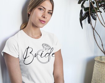 Puede incluir: Camiseta blanca con la palabra "Bride" escrita en cursiva con un gráfico de anillo de diamantes.
