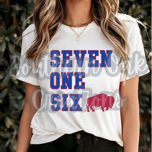 Op de afbeelding: Wit T-shirt met blauwe en rode tekst die "SEVEN ONE SIX" zegt en een rood buffelsilhouet.