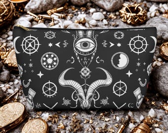 Könnte beinhalten: Schwarze Kosmetiktasche mit goldenem Reißverschluss und weißem Okkultmuster. Das Design umfasst einen Ziegenschädel, ein Auge, einen Mond, Sterne und andere mystische Symbole. Die Tasche ist rechteckig und liegt auf einer Steinoberfläche.