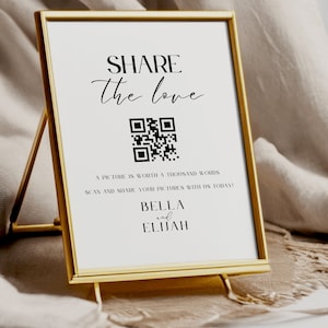 May include: A white sign with black text that reads "SHARE the love" and features a QR code. The text below the QR code reads "A picture is worth a thousand words. Scan and share your pictures with us today! Bella and Elijah."
