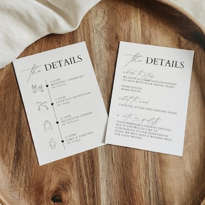 May include: Two wedding details cards with elegant calligraphy on a wooden tray. The cards have the text "The Details" at the top. One card lists the wedding timeline, and the other card lists accommodation and gift information.