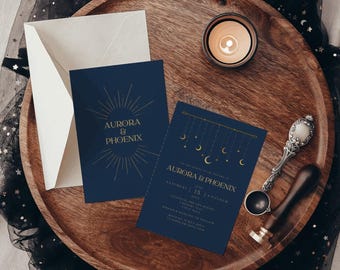 May include: Two dark blue wedding invitation cards with gold foil text and celestial graphics. One card features a sunburst design, the other shows hanging moons and stars. Includes a cream envelope and a metal wax seal stamp tool.