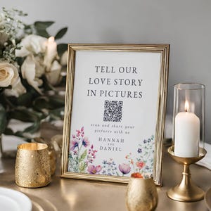 May include: Gold framed sign with the text "Tell our love story in pictures" and a QR code. The sign has a floral design with the names Hannah and Daniel.