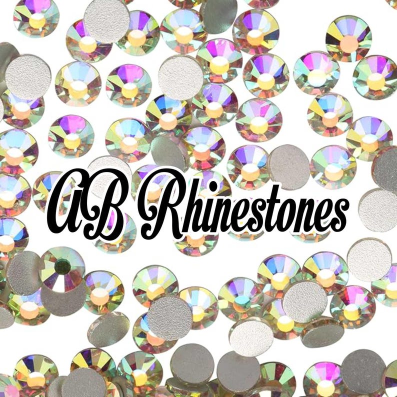 May include: A scattering of iridescent AB rhinestones and silver-backed rhinestones on a white background. The text "AB Rhinestones" is displayed in a black, cursive font.